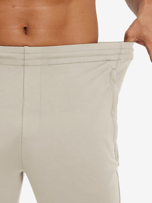 Model stretching waistband to show fit of lightweight traning track pants in khaki.