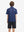 Back half-body view of youth wearing navy colorful flower performance print boys golf polo, showing rear design